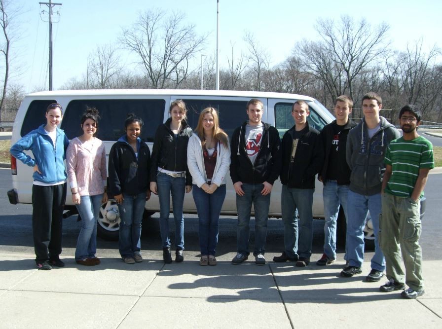 ten students standing in front of a white UC van