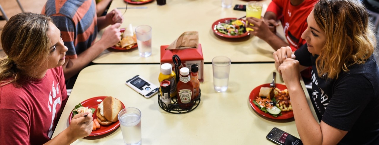 Students sit at a long rectangular table eating and chatting in a University of Cincinnati dining center.