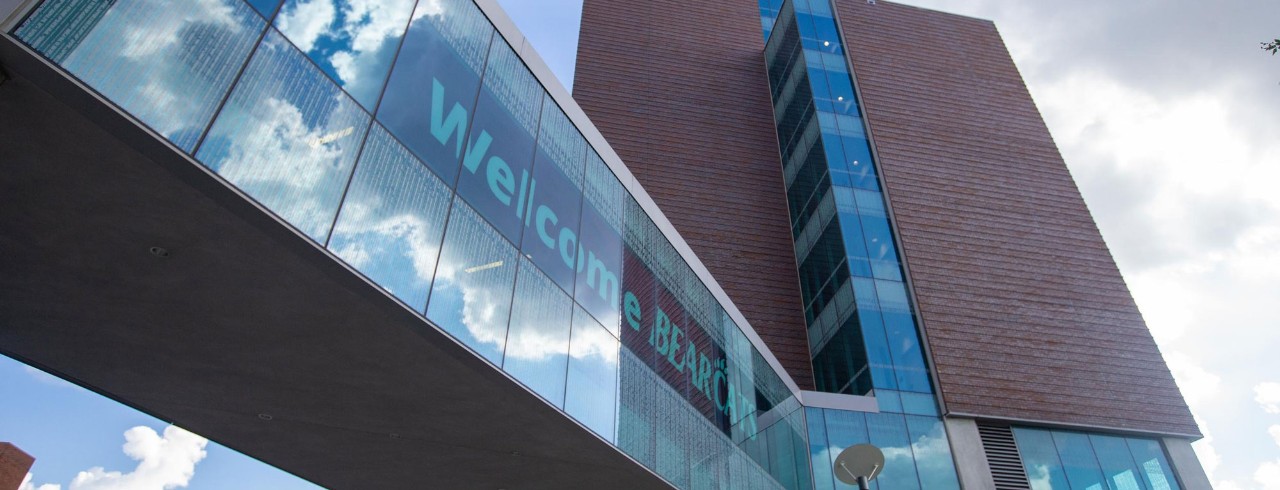 looking up along the side of a building an a walkway with glass windows and a sign reading 'Welcome Bearcats'