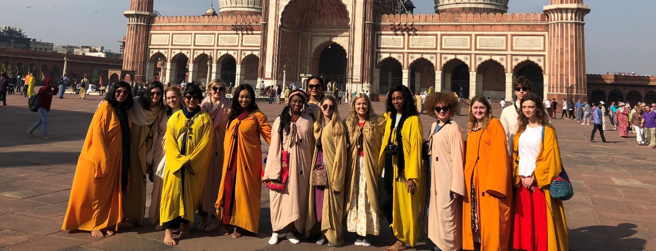 Students in colorful traditional Indian clothes stand in front of a temple.