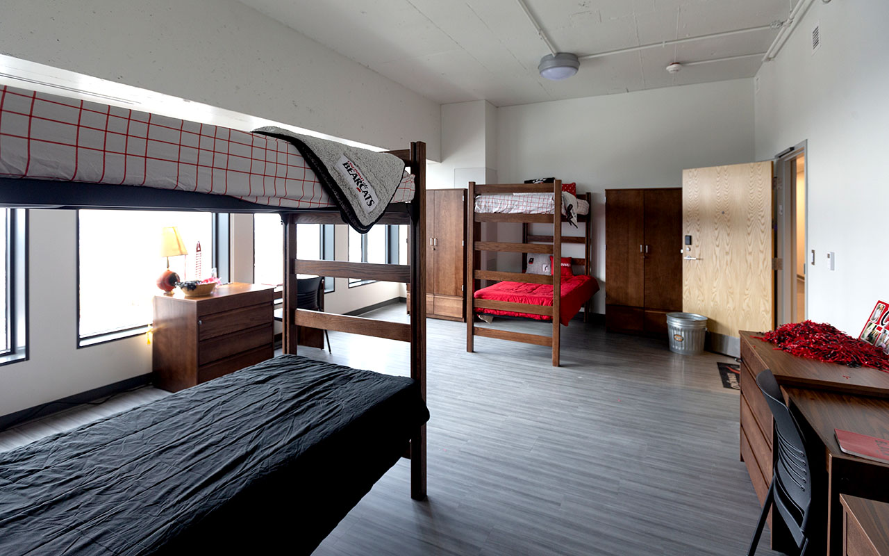 Room with two sets of bunk beds, desks with storage and wardrobes