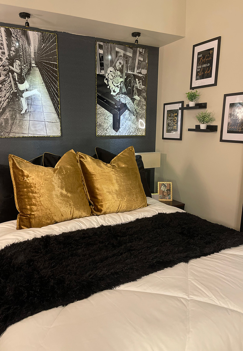 Bed decorated in black and gold with black and white images on the wlal