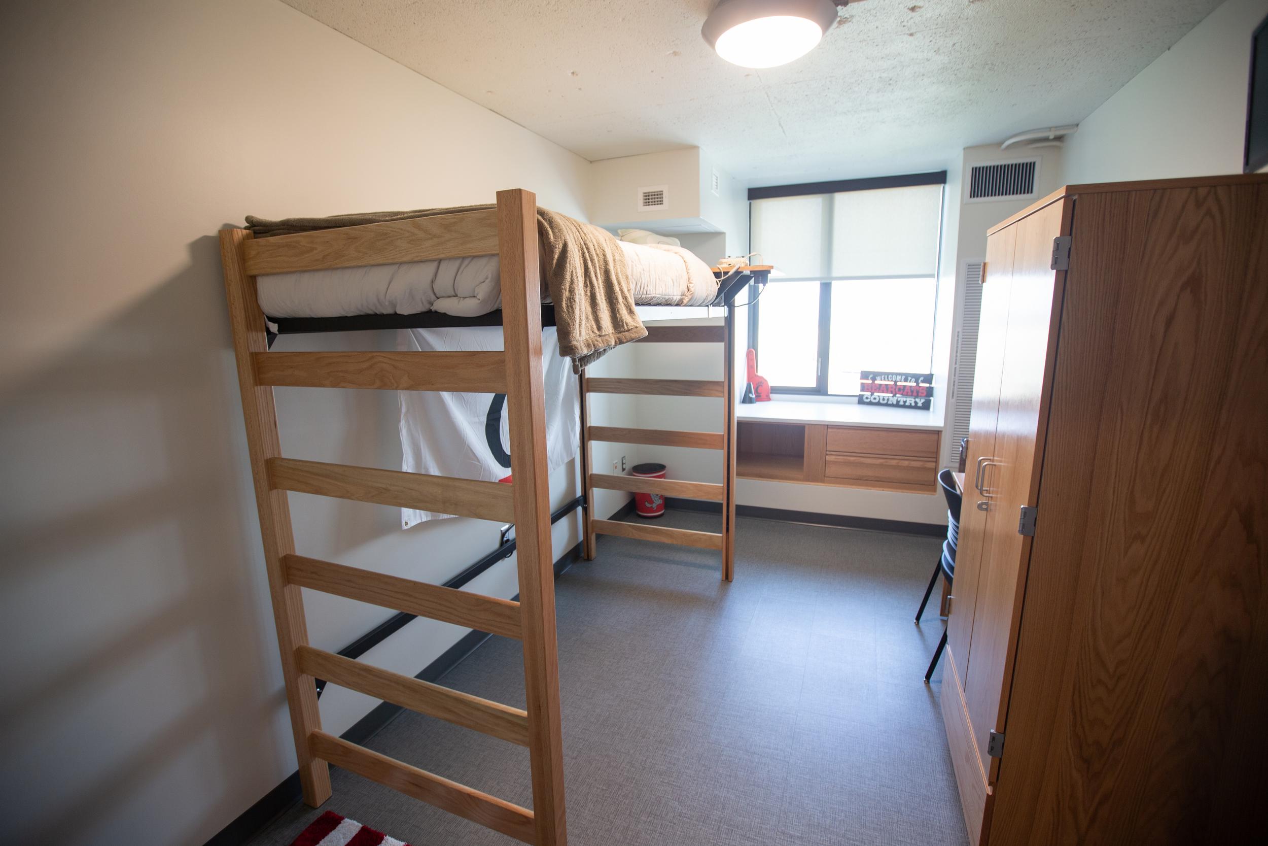 High loft single bunk bed at left, windows and storage at back and wardrobe at right