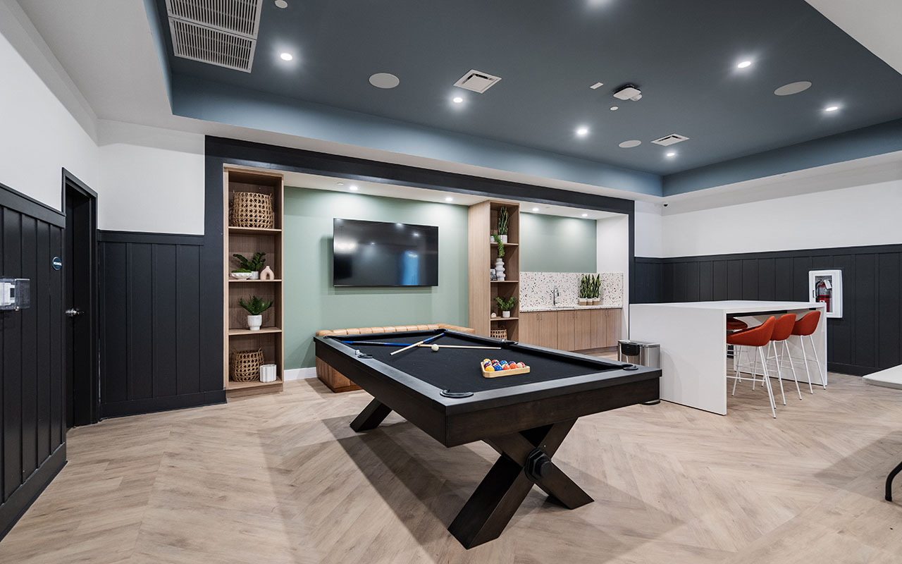 Modern recreation room with pool table, tall worktable and chairs, TV and sink