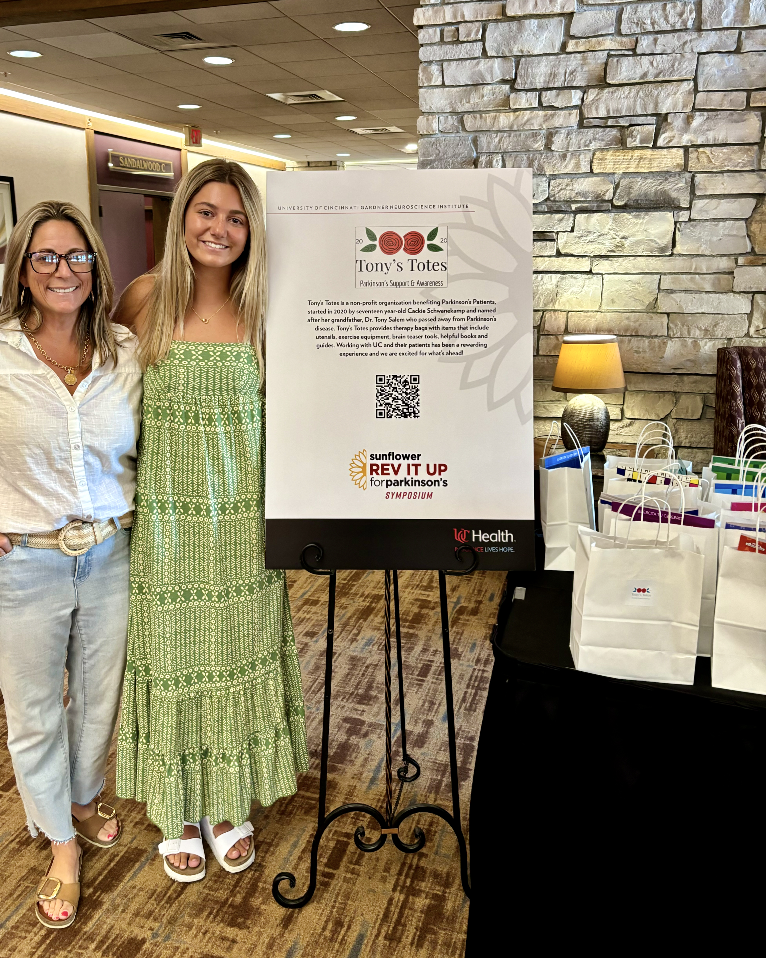 Two women on left stand next to a Tony's Totes poster at a Parkinson's symposium.