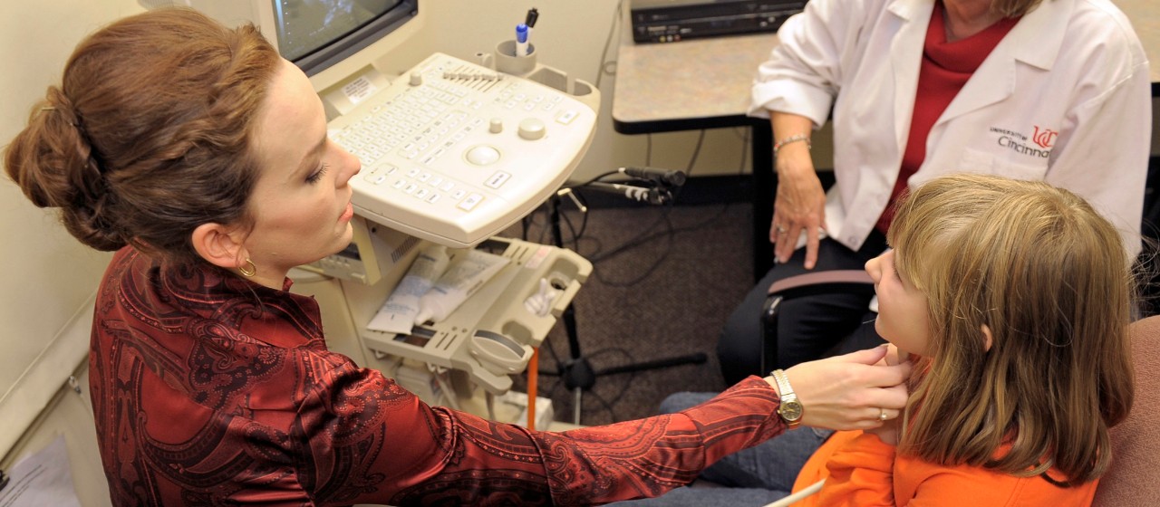 woman holds ultrasound device under a child's chin tracking tongue movements during speech.