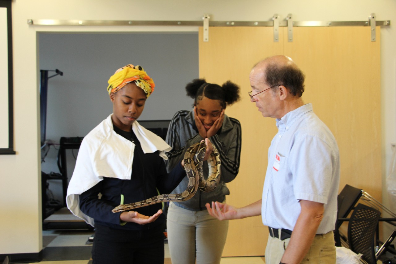 Biology professor Bruce Jayne helps a high school student hold a snake.