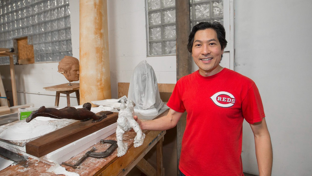 Tom Tsuchiya holds up a scale model of Pete Rose sliding headfirst next to a lifesize cast in his art studio.