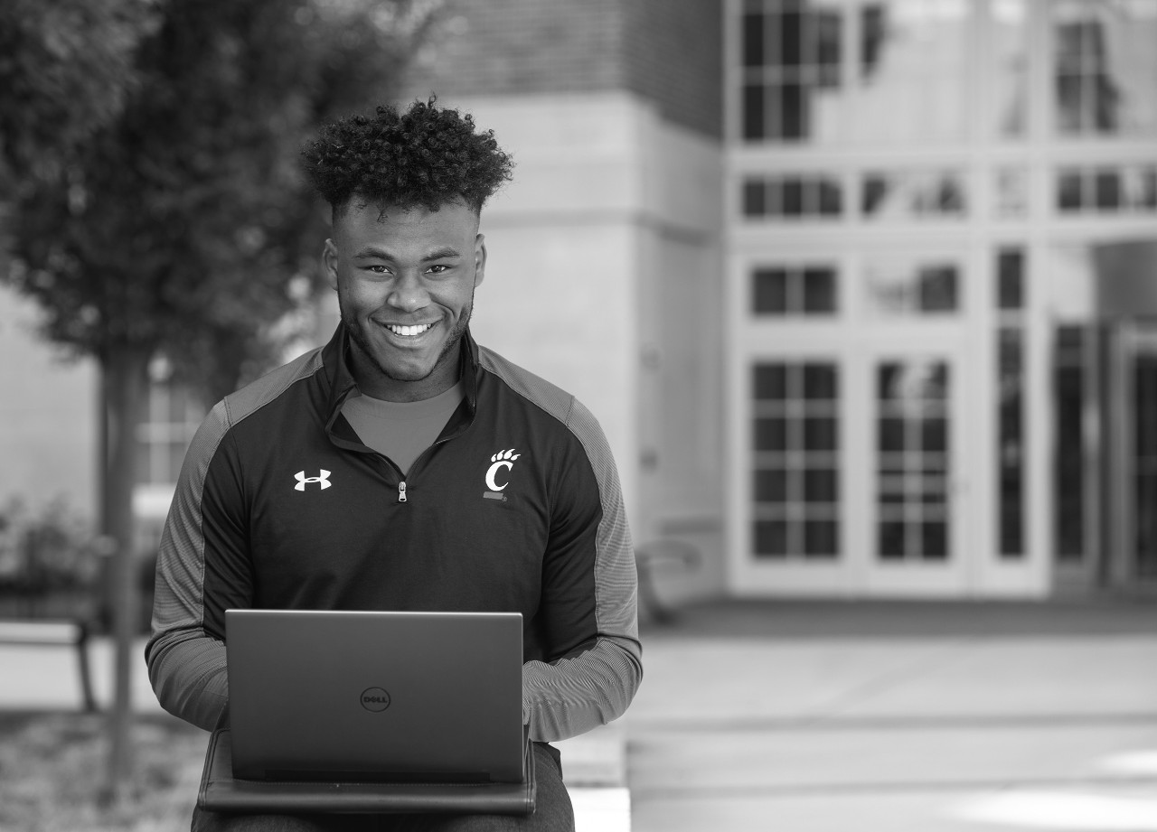 Student poses outside a campus building with laptop