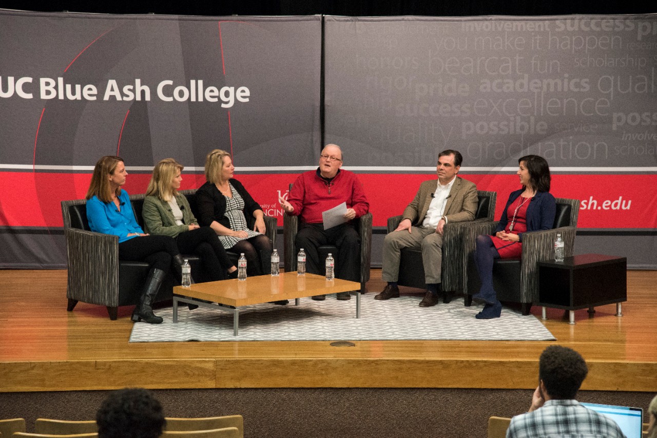 Professor Kent Lutz moderates a discussion on stage with panel speakers