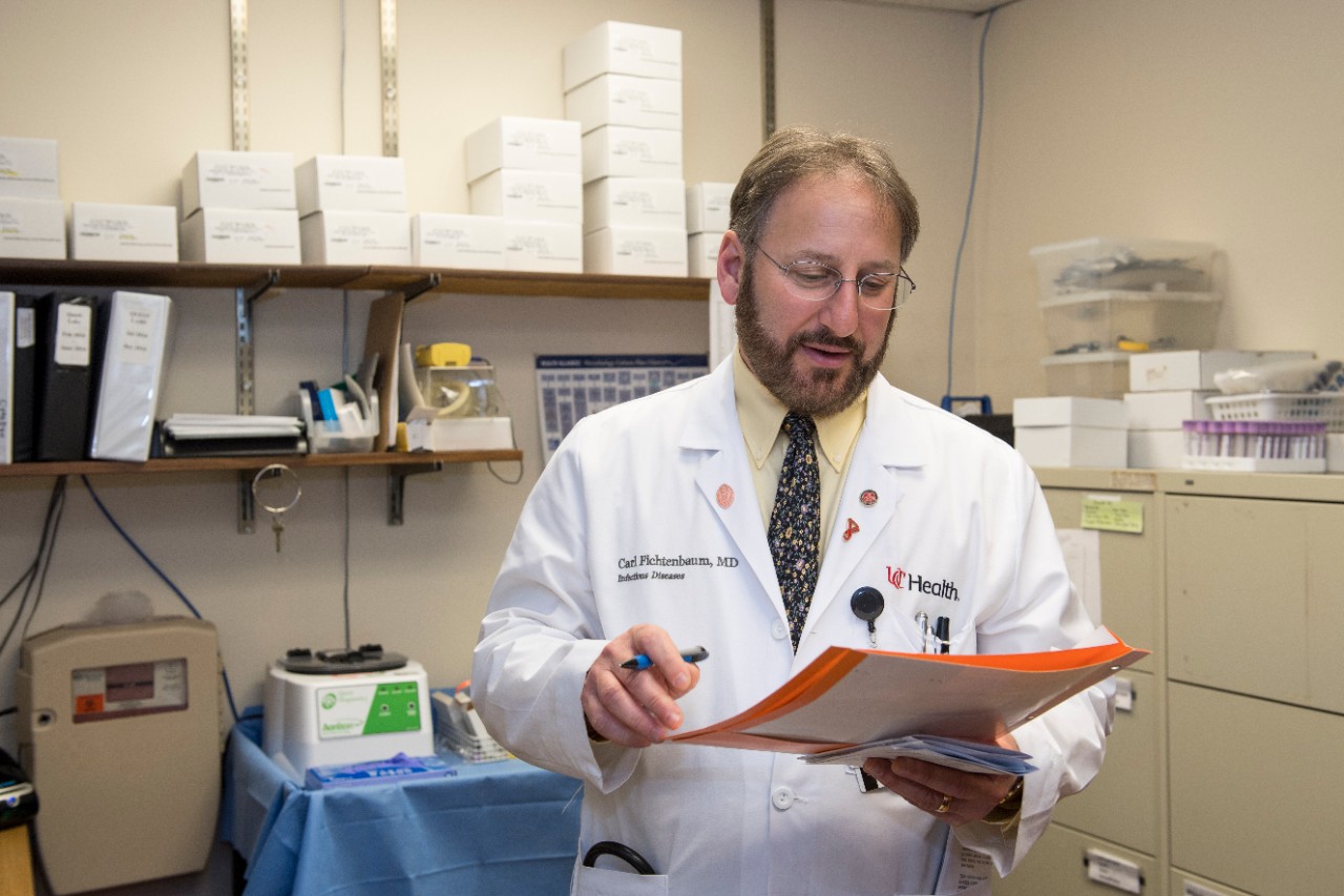 a doctor in a lab coat looks at a file folder he is holding in his left hand