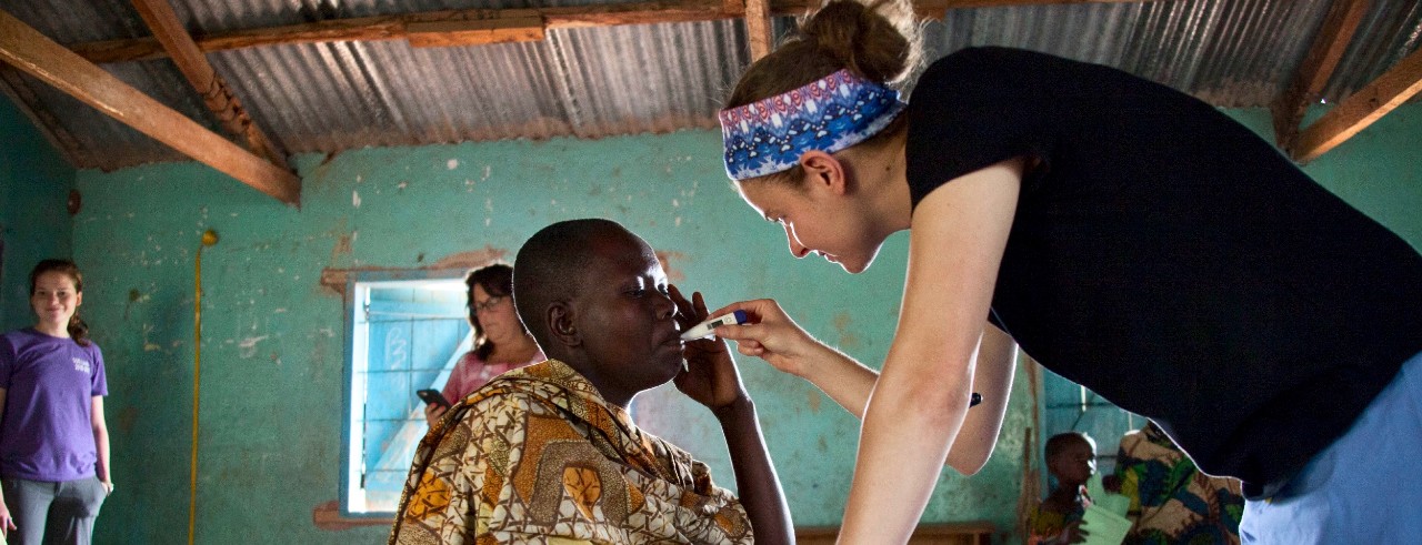 A female medical volunteer leans on a table as she takes the temperature of an African woman.