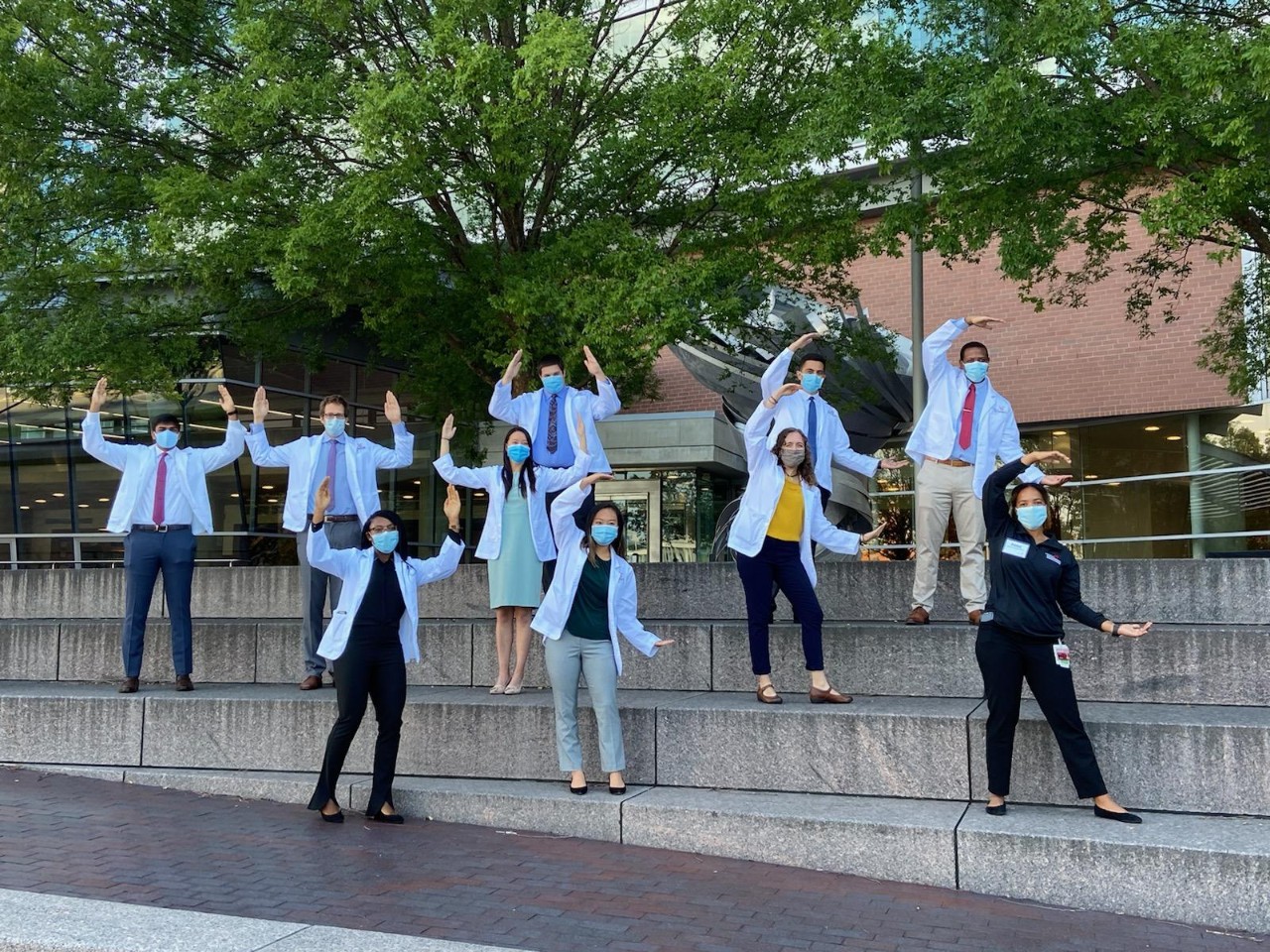 A group of incoming medical students in white coats shown in front of the UC College of Medicine.
