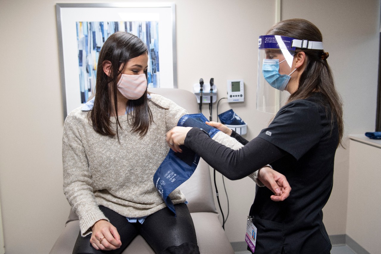 a woman wearing a mask getting her blood pressure taken by a hospital staffer