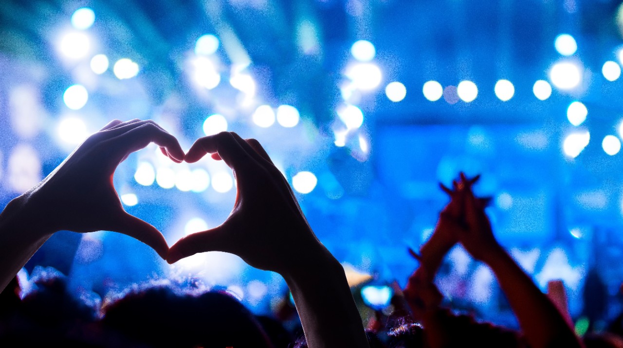 A concertgoer makes a heart shape in front of blue mood lighting at a concert.