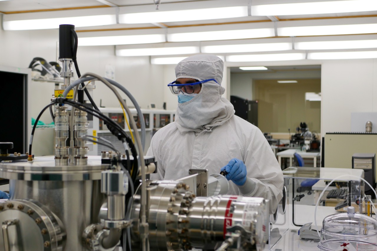 A UC student wearing protective clothing from head to toe works in a clean room.