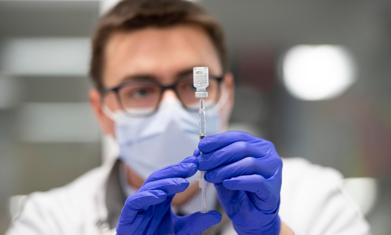 A UC College of Pharmacy student in a facemask and gloves draws a syringe.