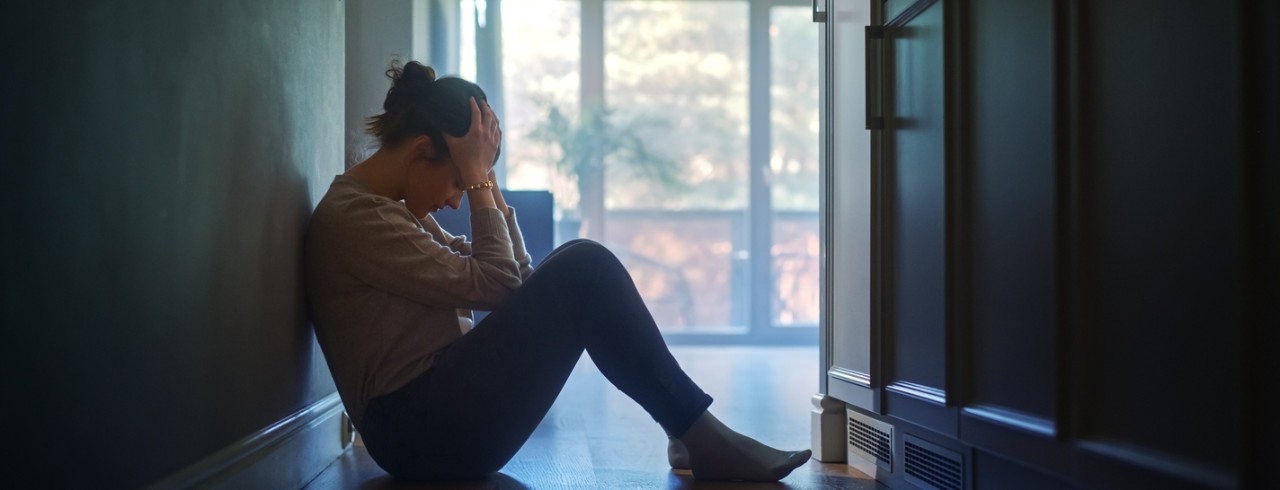 A woman sits on the floor with her head in her hands.