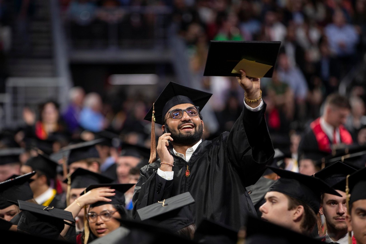 A UC graduate in his cap and gown waves to supporters in the stands at Fifth Third Arena.