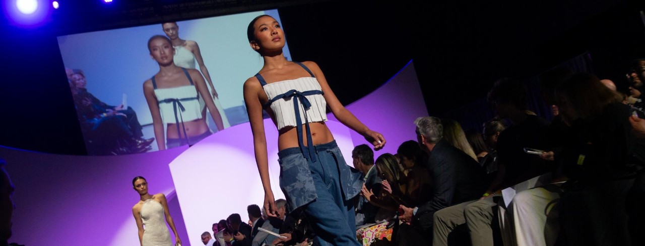model walking on the runway with a white top with blue ribbons and jeans 