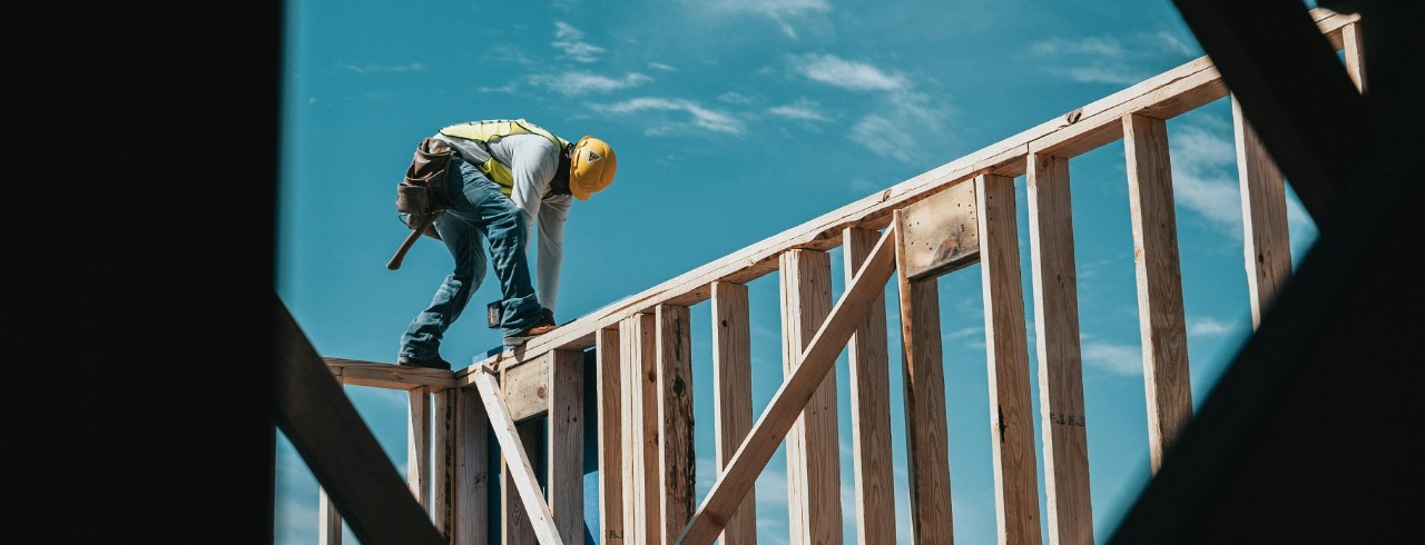 A man stands atop a wall of 2x4s as he constructs a home.