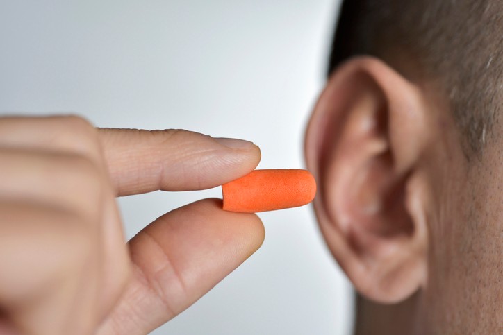 A person holds an orange ear plug up to their ear