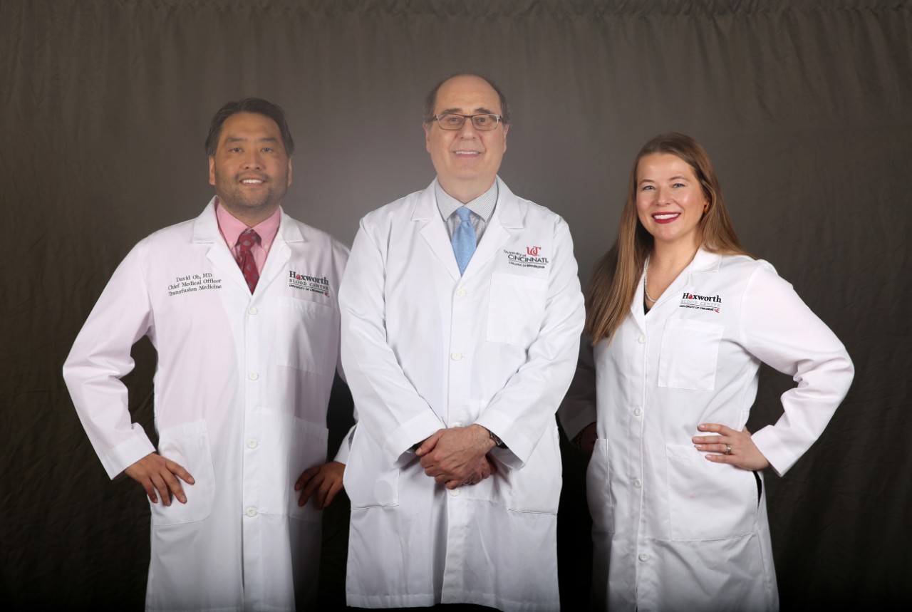 Three doctors stand smiling while wearing lab coats