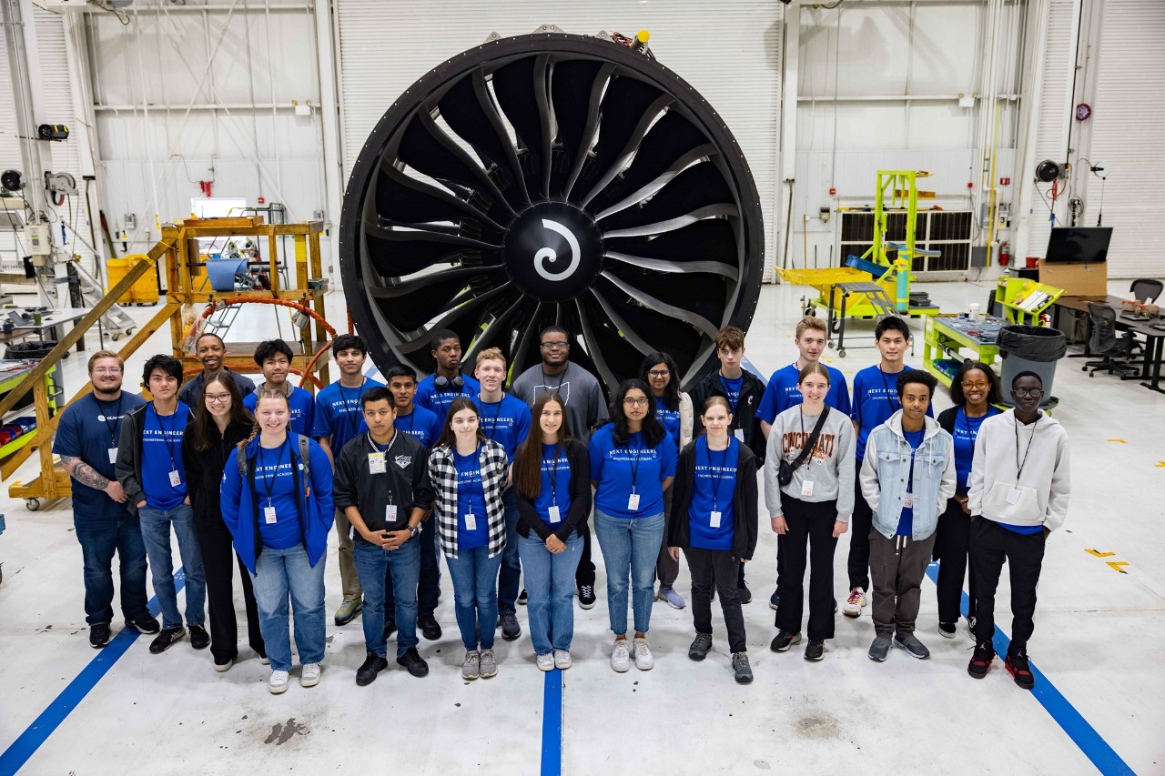 High school students pose in front of an enormous jet engine.