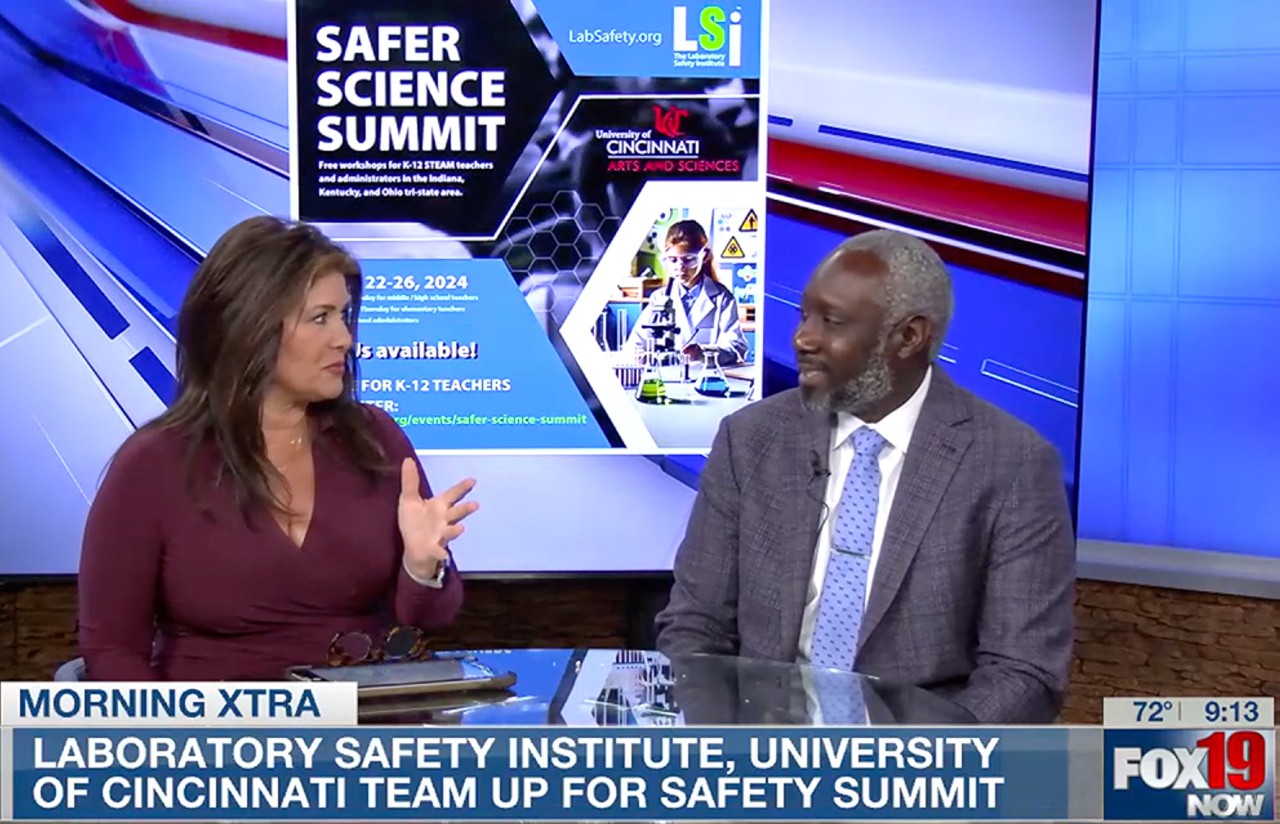 Morning host Julie O'Neill talks to James Mack at the anchor desk in front of a banner for the Safer Science Summit.