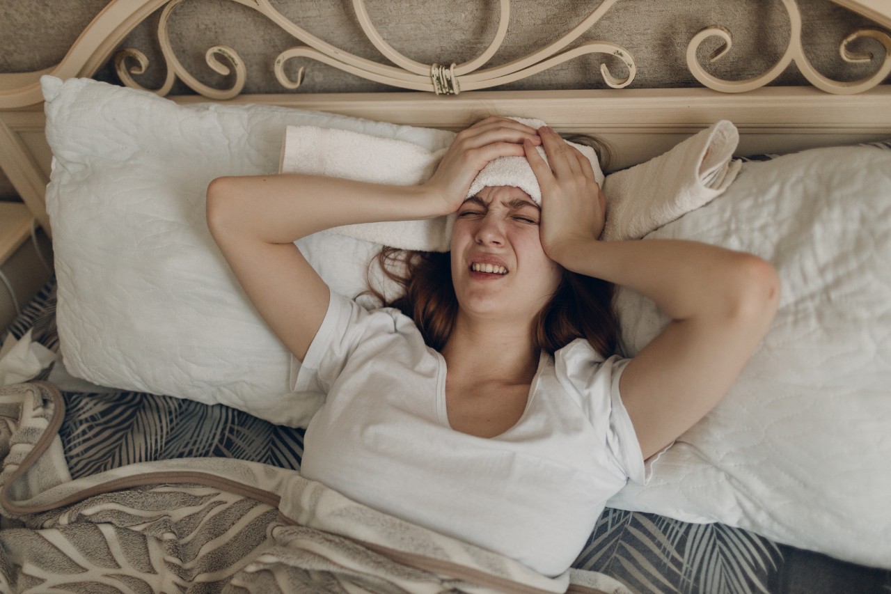 stock image of a woman with a headache gestering with hands on side of her face in bed