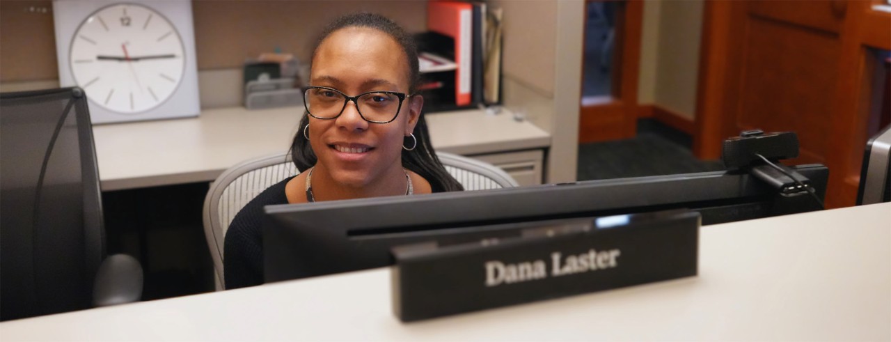 young woman sits at desk with a name block that reads Dana Laster