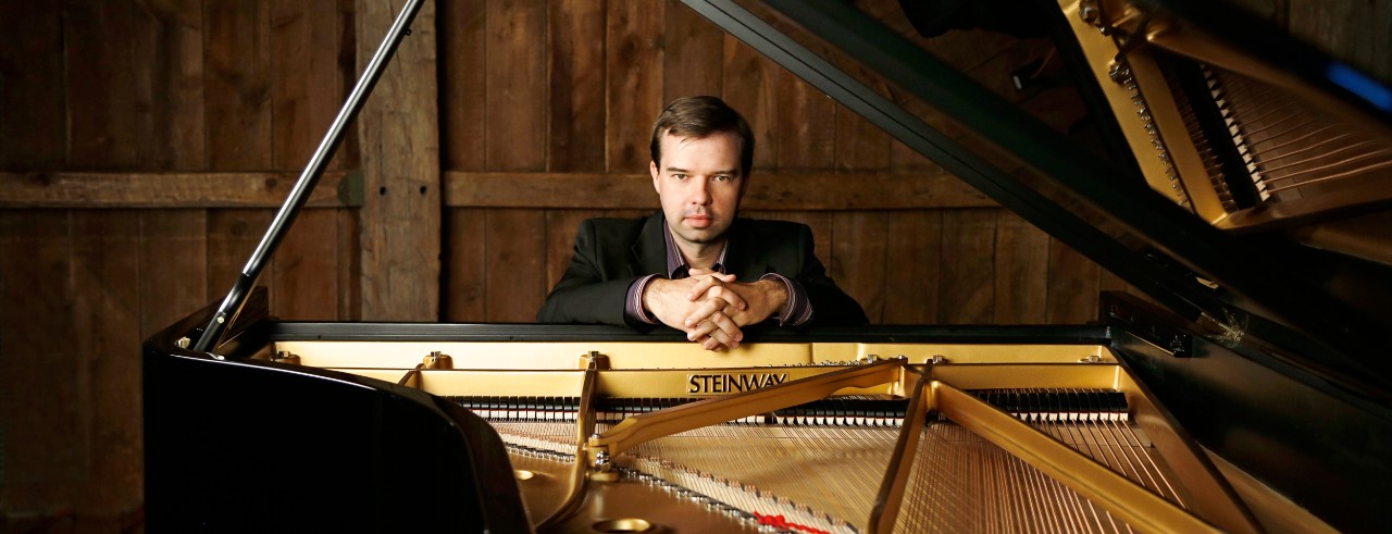 A portrait of new CCM faculty member Kirill Kuzmin seated at a Steinway piano. Photo/Kristin Hoebermann