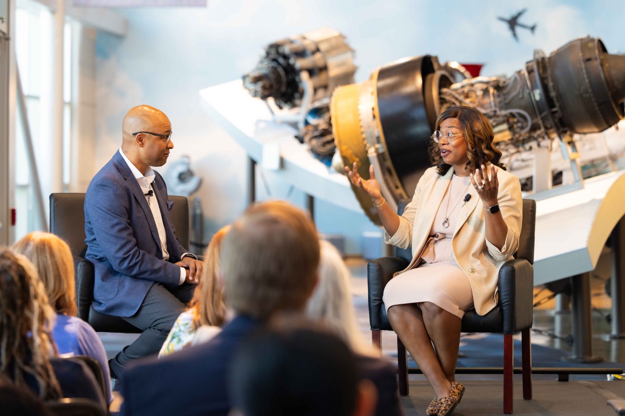 Whitney Gaskins and Germaine Hunter talk at a public event in front of a GE jet engine.
