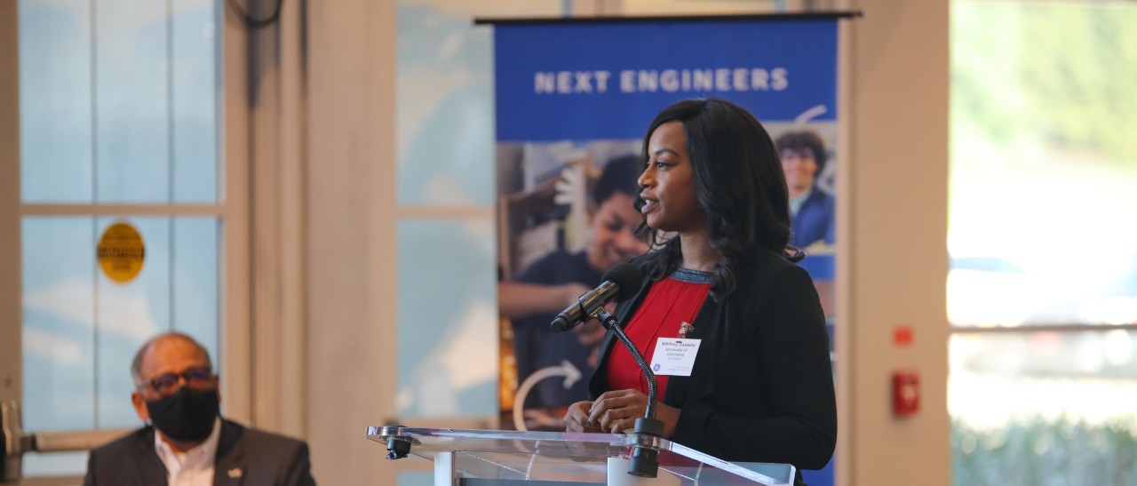 UC Associate Dean Whitney Gaskins speaks at a lectern at GE Aerospace in front of a sign reading "Next Engineers."