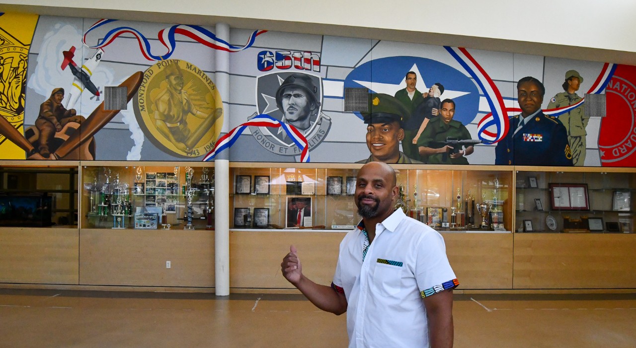 UC grad Brandon Hawkins stands in front of his mural featuring stories of the military.