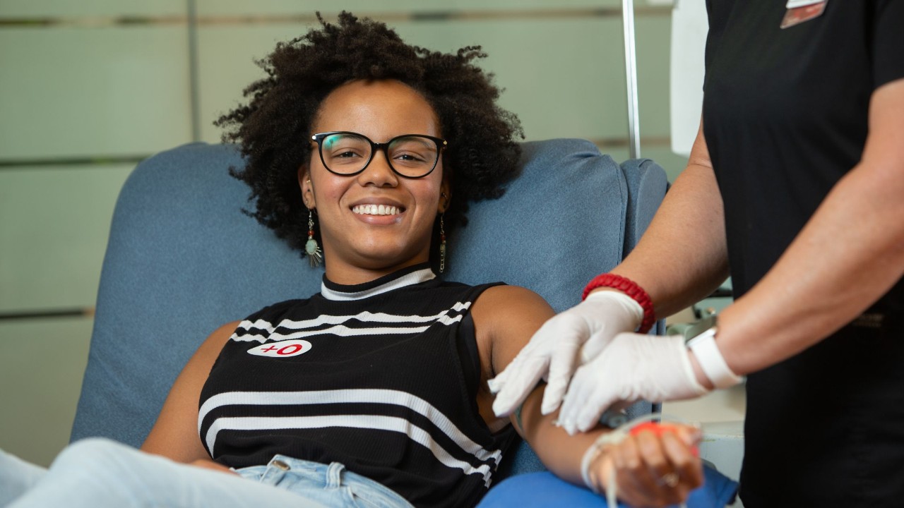 A woman smiles while a technician prepares her arm to give blood