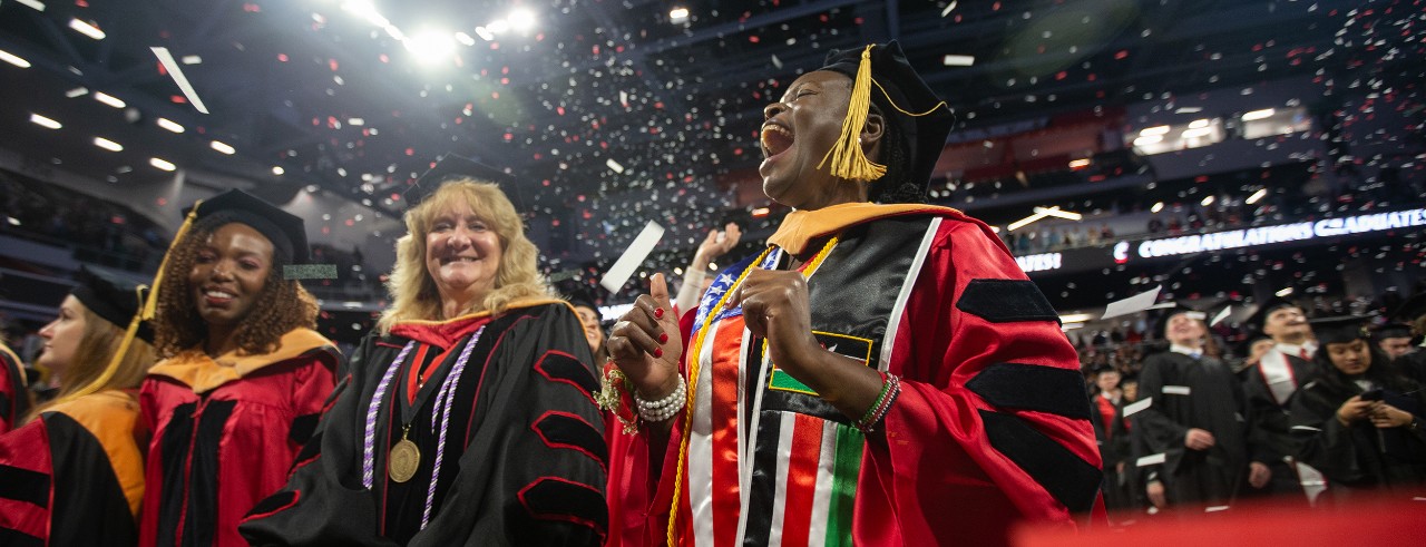 UC graduates in caps and gowns celebrate commencement as confetti falls from the rafts of Fifth Third Arena.