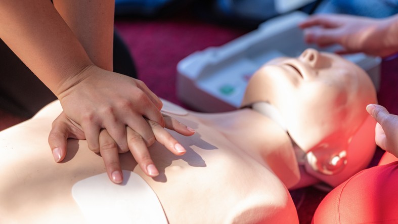 A person places their hands on the chest of a CPR dummy during a training session