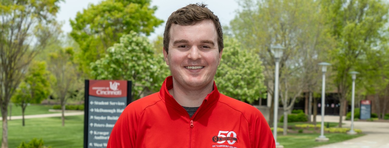 UC Clermont graduate Nathan Gorman stands on campus in front of college signage. 