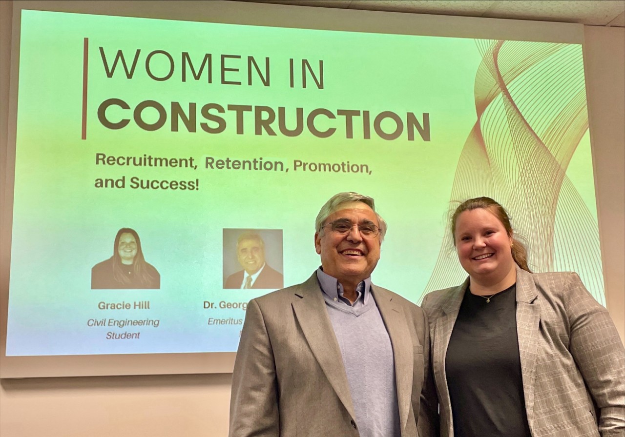 Gracie Hill and George Suckarieh pose in front of a presentation screen 