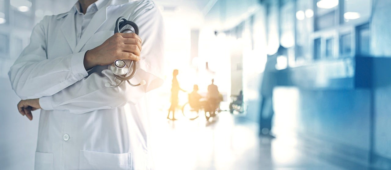 A doctor in a white coat stands in the hallway of a hospital. 