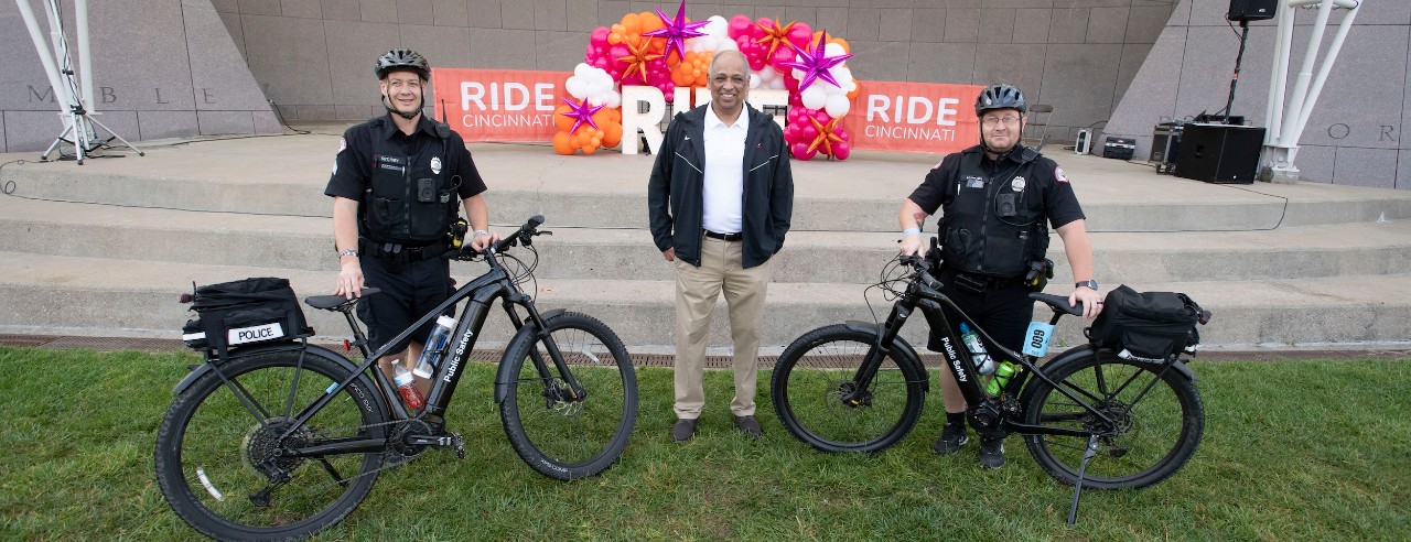 President Pinto stands with Ride Cincinnati participants near stage with balloons and sign