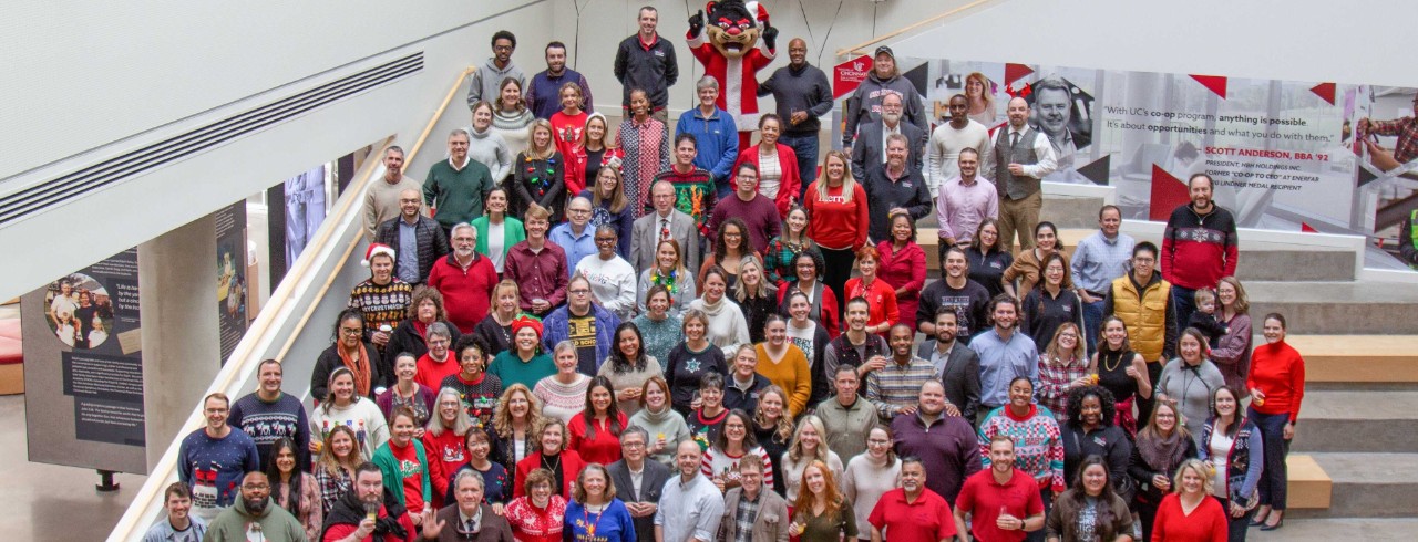 A crowd of Lindner faculty and staff gather on the Lindner Hall atrium steps in festive holiday clothing