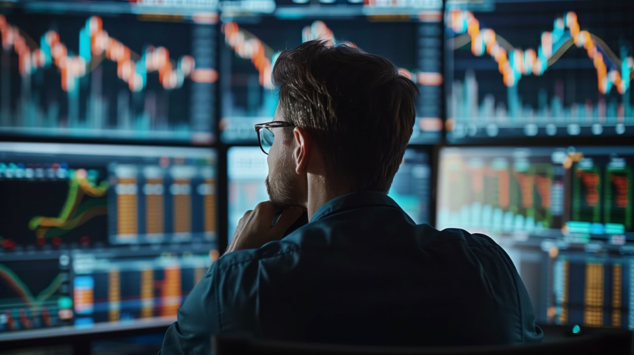 A man in glasses looks at screens with financial data.