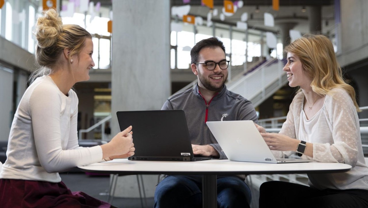 three students working at a table with laptops