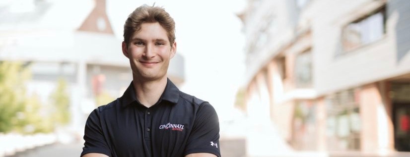 A UC student stands outside in front of a building.