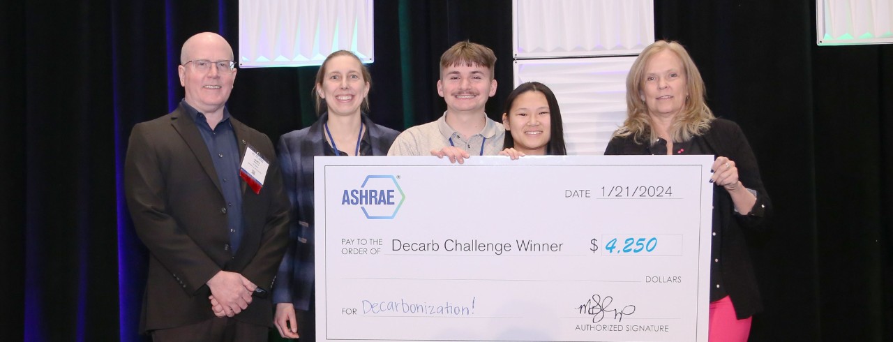 a group of 5 people smile and hold a giant check on stage. 