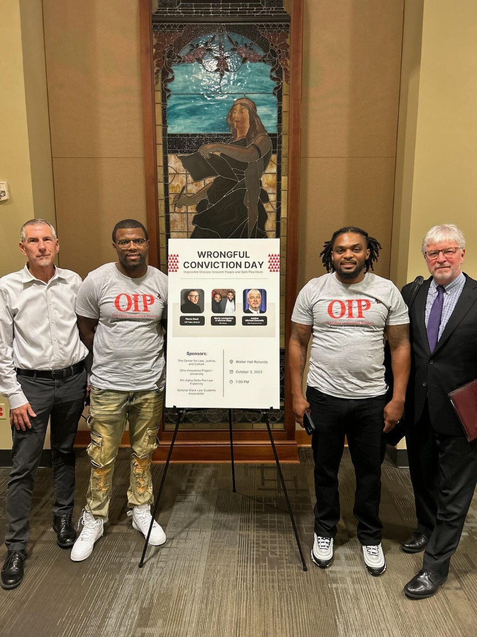 Four men, with two standing on either side of a wrongful conviction day sign. Marcus Sapp is among those standing