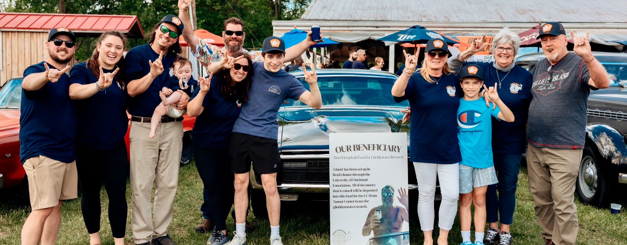 Several men and women stand around a sign promoting the "Brad to the Bone" fundraising event for brain cancer research.