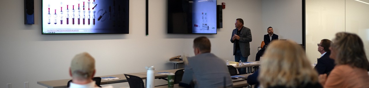 Exit Lab participants look forward at a screen with a presentor standing by.